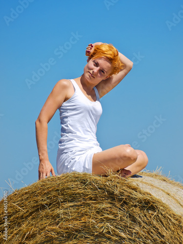 Young woman on the big hay bale roll