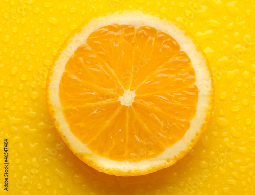 Slice of orange with drop on yellow background