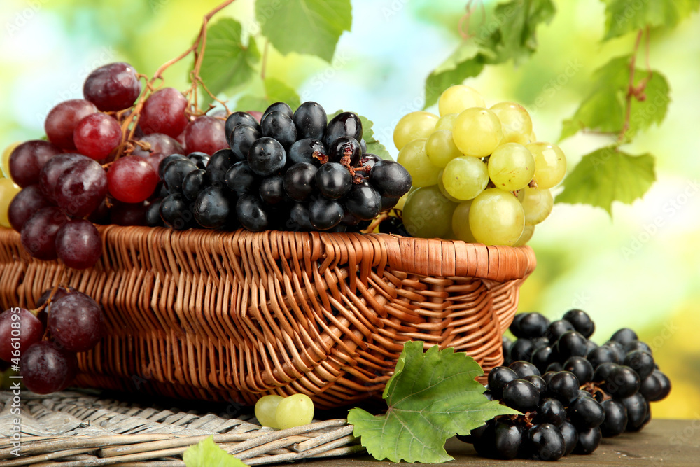 assortment of ripe sweet grapes in basket, on green background assortment of ripe sweet grapes in basket, on green background