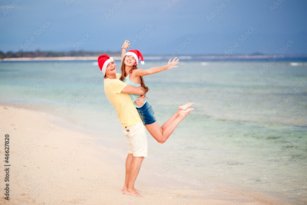young couple in santa hats laughing on tropical beach. new year young couple in santa hats laughing on tropical beach. new year