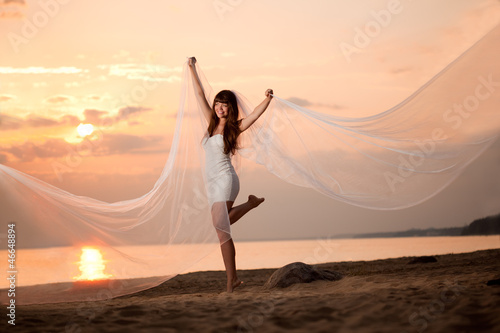Beautiful bride with a long veil on the beach at sunset