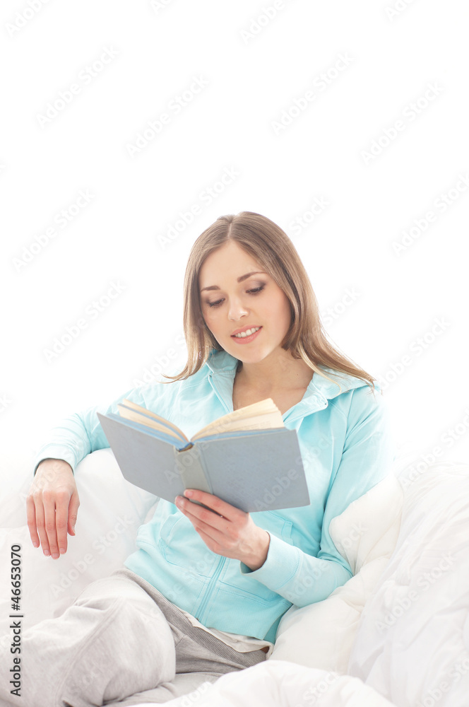 Fototapeta premium A young brunette woman reading a book on a white sofa