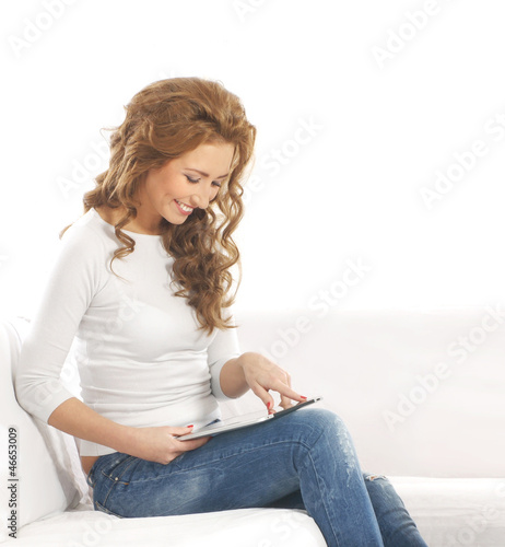 A young and happy woman with a tablet relaxing on a white sofa