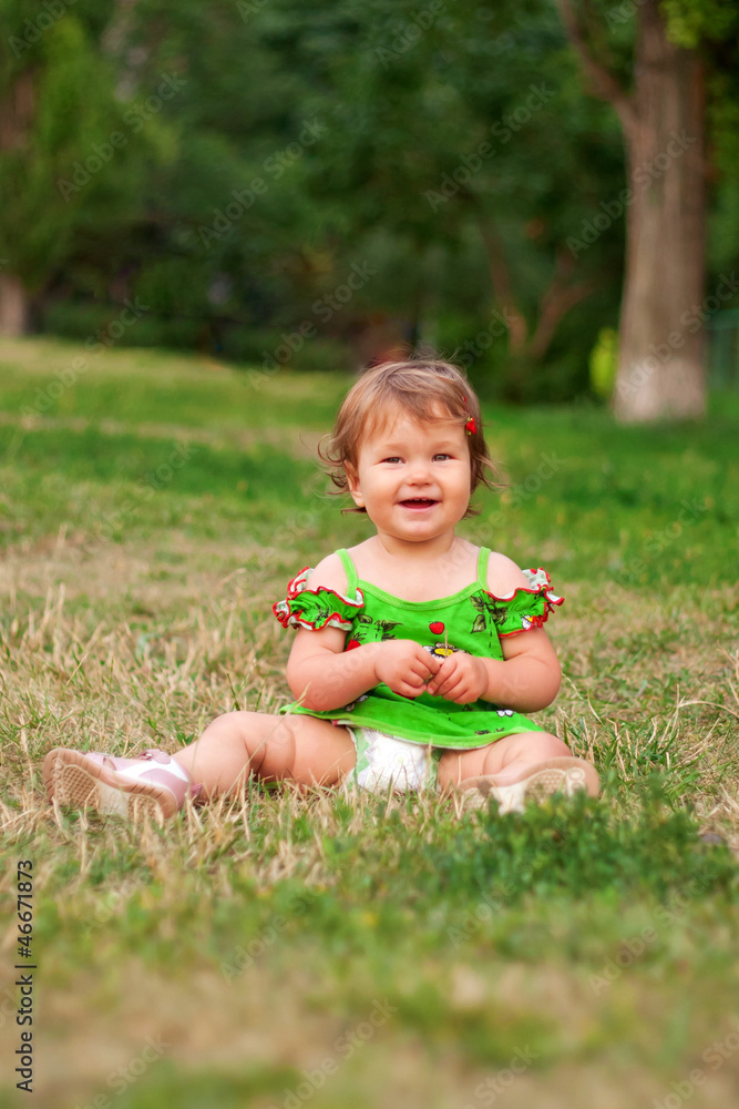 baby girl sitting on the green grass in the park and smiling baby girl sitting on the green grass in the park and smiling