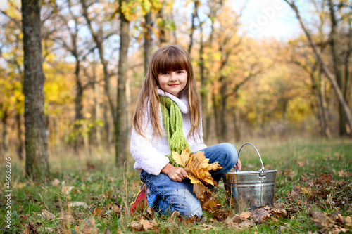 Smiling girl with maple leaves and a bucket outdoors