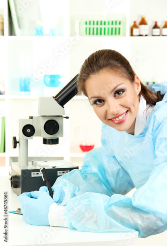 Young scientist looking into microscope in laboratory.