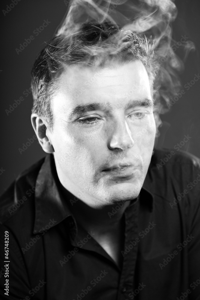 Obraz premium Smoking man with short brown hair. Black and white studio shot.