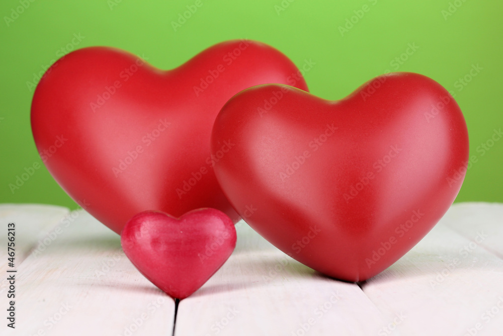 Decorative red hearts on white wooden table on green background Decorative red hearts on white wooden table on green background