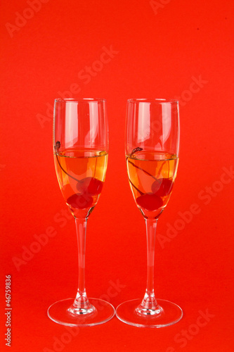 two glass goblets with champagne on red background