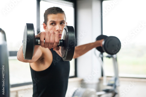 Young man exercising with dumbbells in a gym, focus on weight.