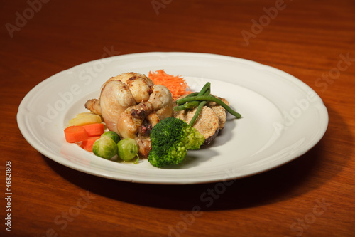 Dinner of vegetables and chicken on a plate and wooden table.