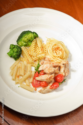 Dinner of vegetables pasta tomato and chicken on a white plate.