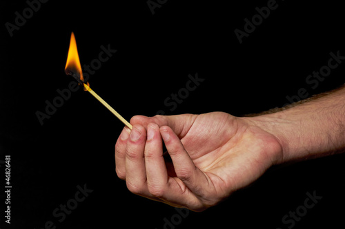 Hand holding burning match stick on black background