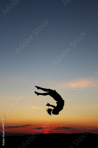 silhouette of female gymnast doing a somersault in sunset