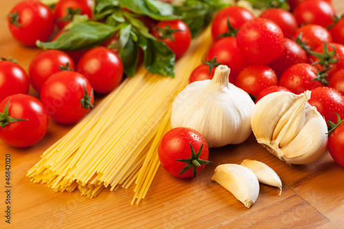 Pasta, tomatoes, garlic and basil on wooden table