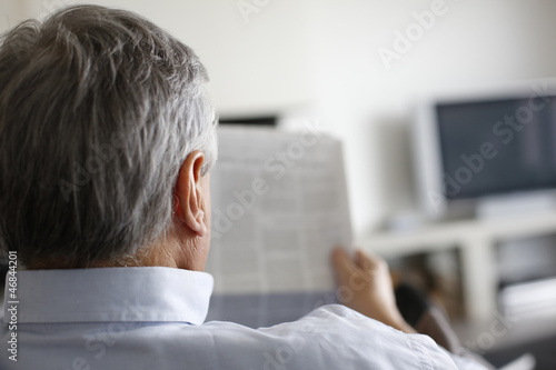 Back view of man reading newspaper at home