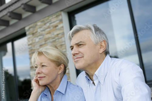 Senior couple sitting in front of house and looking away