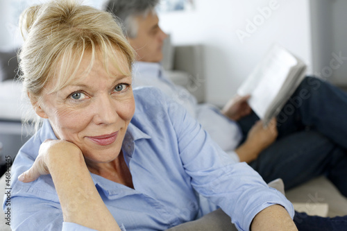 Foto Senior woman sitting in couch, husband in background