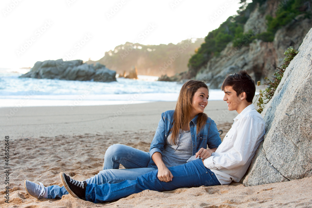 Young handsome couple sitting on beach.