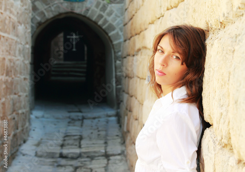 young girl in a white shirt is standing against a stone wall. In © dubova