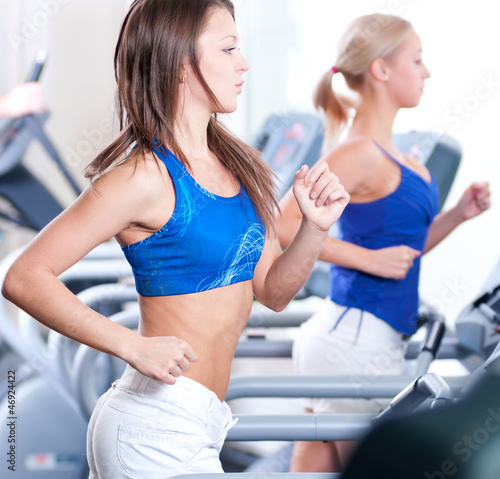 Two young women run on machine in the gym