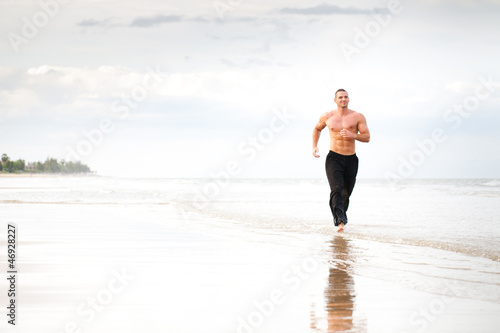 Young handsome muscular man running on the beach