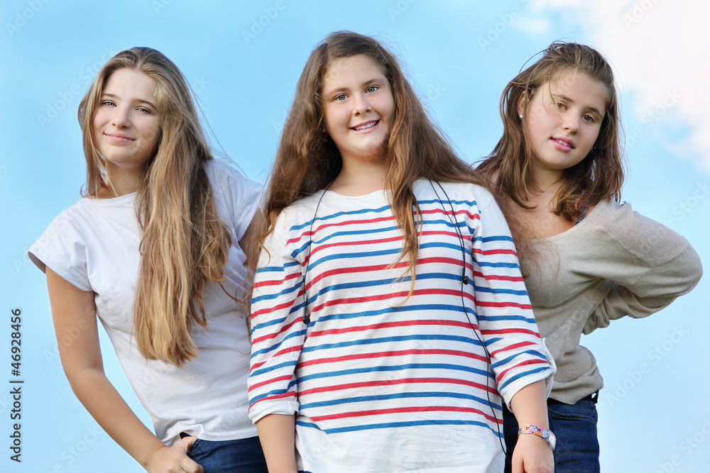 Three happy girls stand together at background of blue sky Three happy girls stand together at background of blue sky