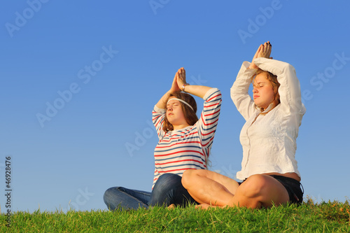 Two young girls meditate at green grass at background of sky photo