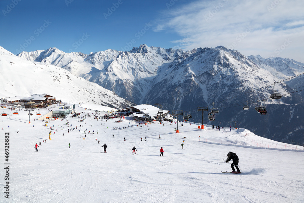 Cable car, buildings in mountains. Many skiers ride in Alps