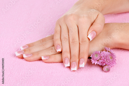 Woman hands with french manicure and flowers on pink towel