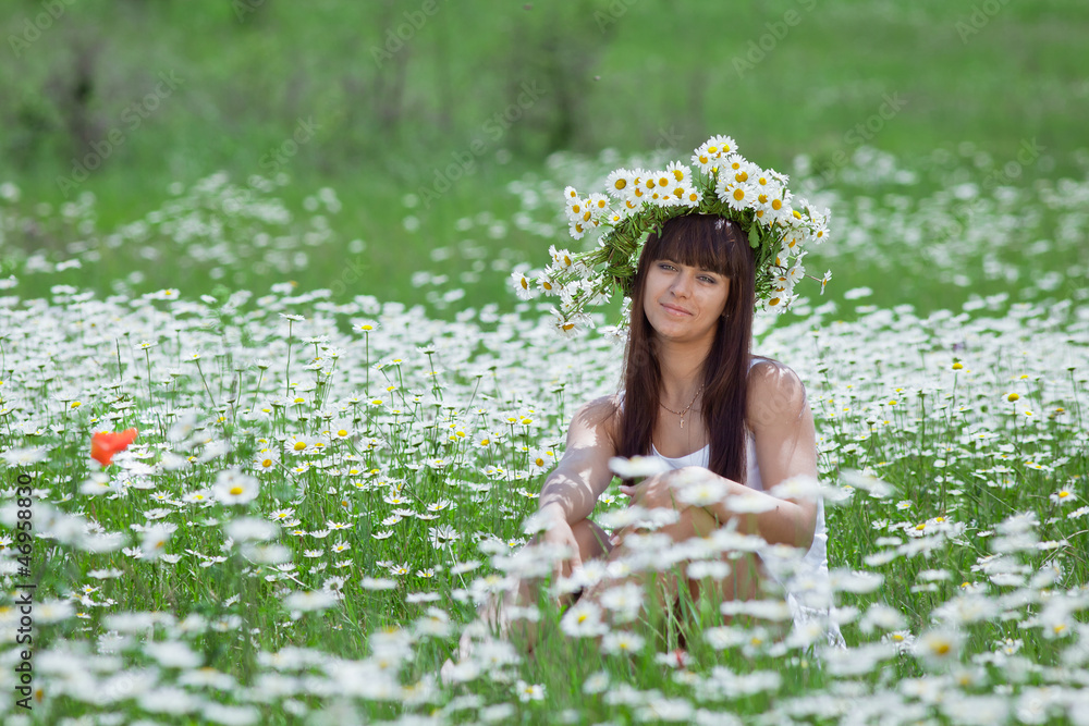 Fototapeta premium Young woman in camomile wreath looking at camera smiling