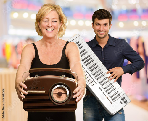 Woman Holding Radio Infront Of Man Holding Piano photo