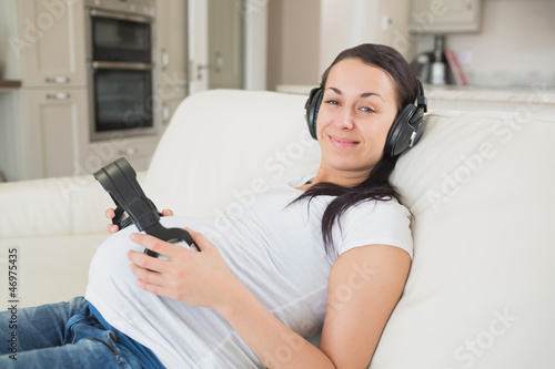 Prospective mother lying on the couch listening to music and hol