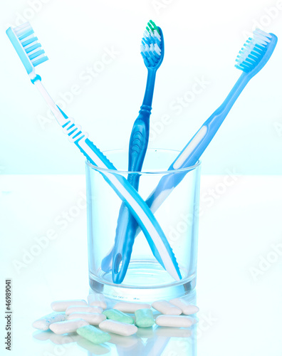 Toothbrush in glass and chewing gum on blue background
