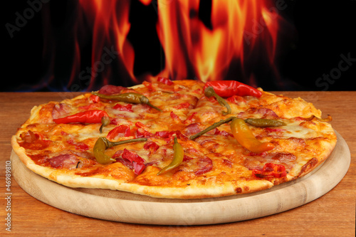 Tasty pepperoni pizza on wooden board on flame background