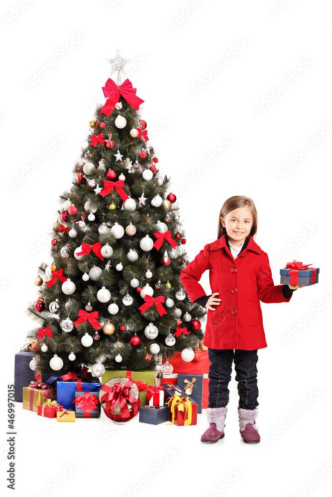 Happy girl standing next to a christmas tree and holding present Happy girl standing next to a christmas tree and holding present