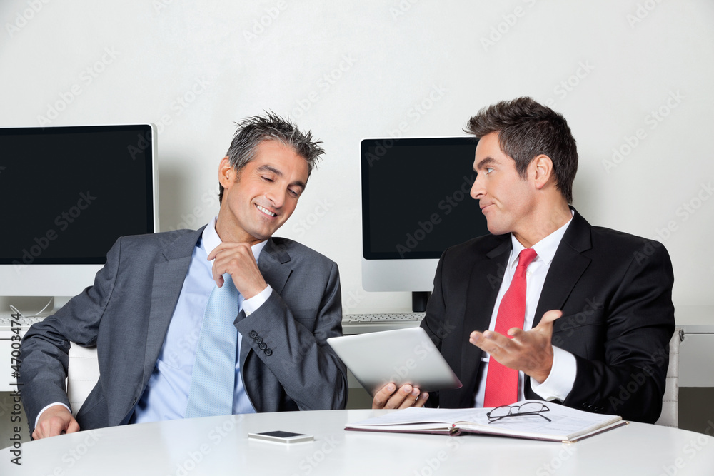 Businessman Holding Digital Tablet Sitting With Colleague At Des Businessman Holding Digital Tablet Sitting With Colleague At Des
