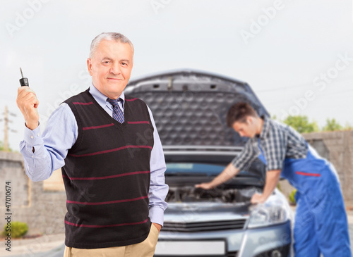 Mature gentleman holding a key while in the background mechanic