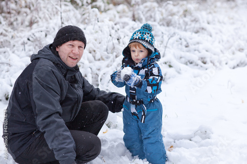 Father and toddler boy having fun with snow on winter day