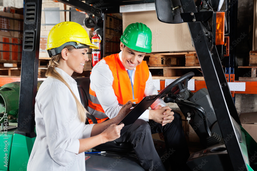 Supervisor Showing Clipboard To Colleague Sitting In Forklift Supervisor Showing Clipboard To Colleague Sitting In Forklift