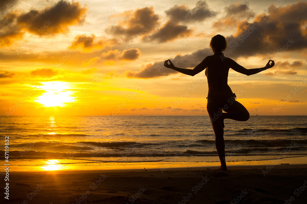 Young woman practicing yoga on the beach at sunset