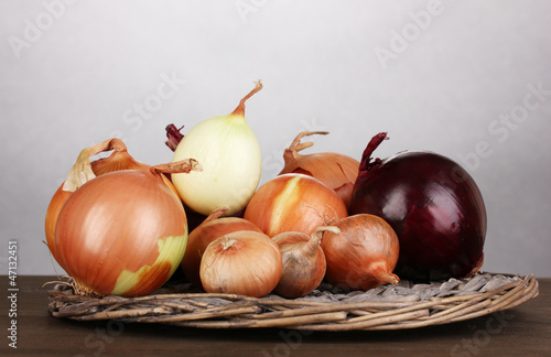Ripe onions on wicker cradle on wooden table on grey background