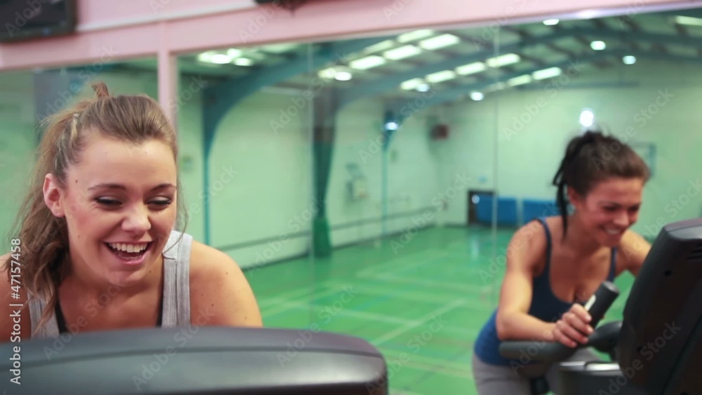 Women cycling on exercise bikes and chatting Women cycling on exercise bikes and chatting
