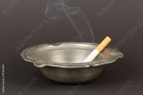 Burning cigarette in an old tin ashtray