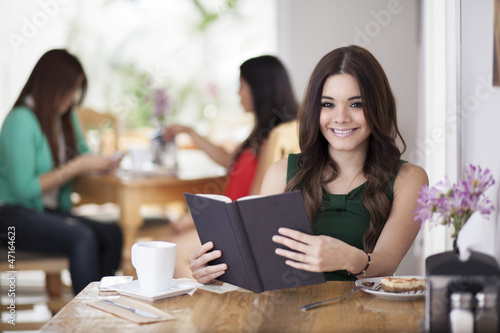 Cute young woman reading and drinking coffee