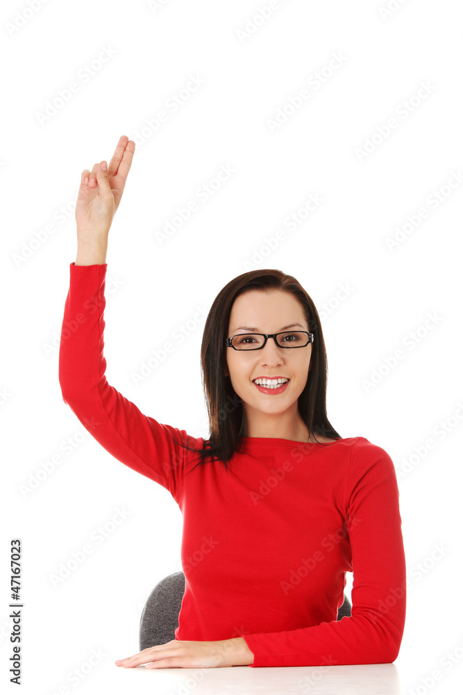 Young woman sitting at the desk with hand up Young woman sitting at the desk with hand up