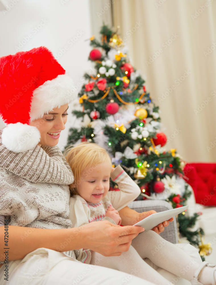 Happy mother and kid using tablet PC near Christmas tree Happy mother and kid using tablet PC near Christmas tree