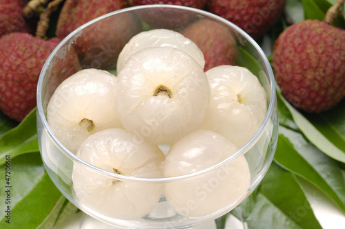 Bowl of peeled lychee with leaf on white