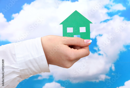 concept: woman hand with paper house on sky background, close