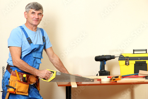 Builder sawing boards on table on wall background